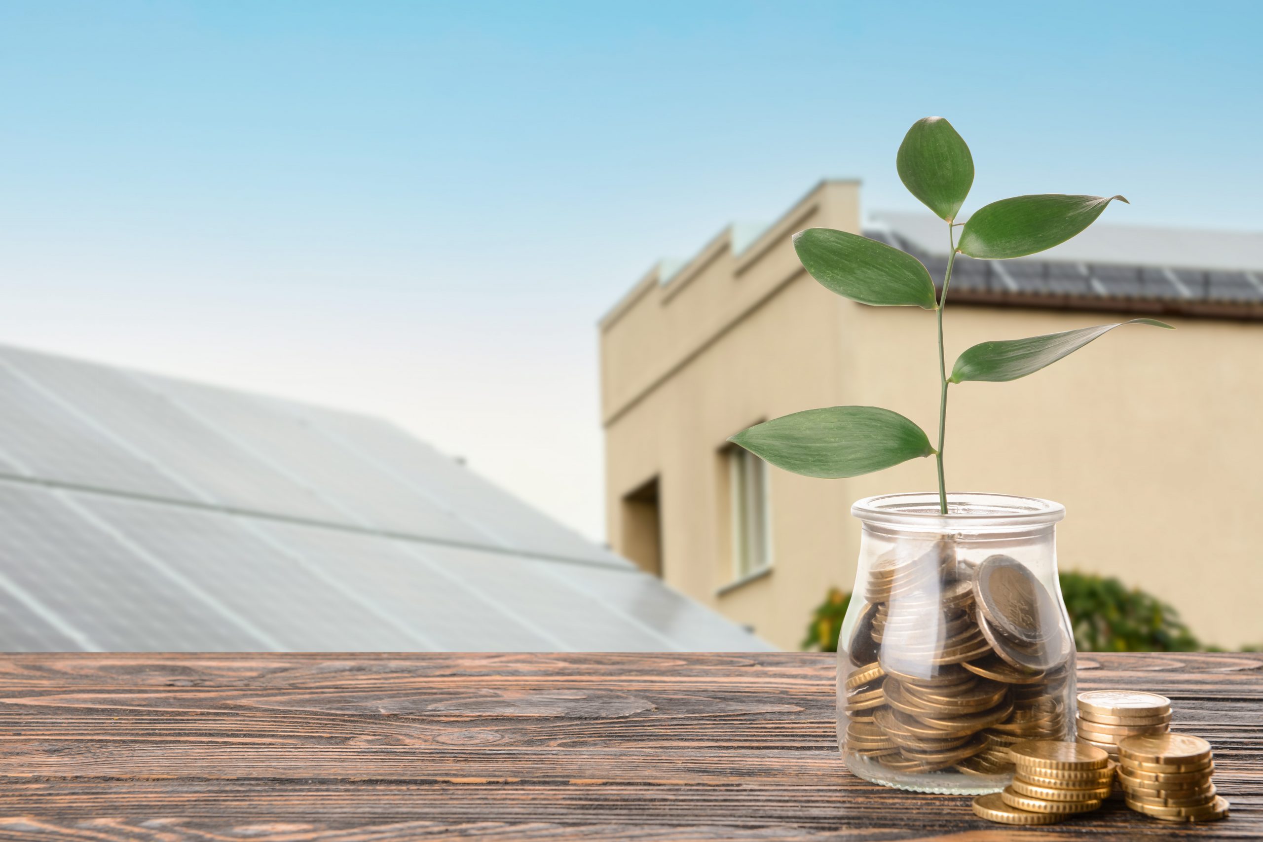 Jar with coins on table near modern solar panels outdoors